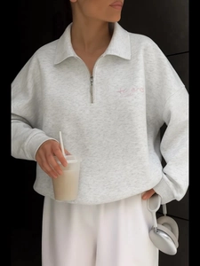 Detail of pink embroidered letters on a light grey half-zip sweatshirt with a high collar