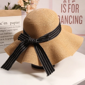 Detail of a woven straw sun hat with a large wavy brim and black striped ribbon bow