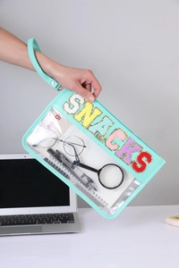 Detail of mint green PVC toiletry bag with SNACKS sequin embroidery and leather trim