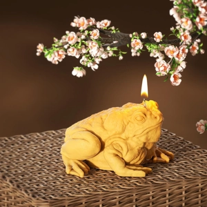 Detailed view of a golden toad-shaped candle burning on a rustic woven surface