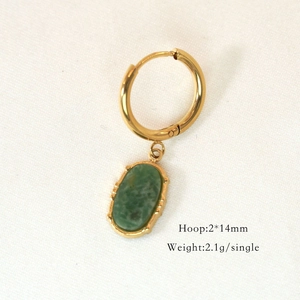 Detail of a gold hoop earring with a green oval gemstone pendant on white fabric
