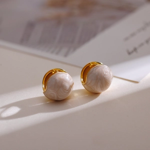 Detail view of French retro earrings with gold metal balls and white marble oil-drop texture