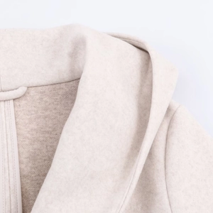 Detailed close-up of soft oatmeal wool texture and stitching on the hooded coat neckline