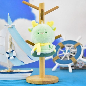 Close-up of a cute green plush dragon keychain with yellow scarf on a wooden stand