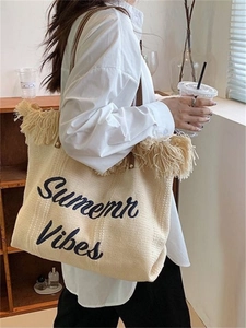 Detail of beige woven tote bag with fringe trim and Summer Vibes lettering on the front