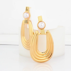Macro view of gold-plated U-shaped drop earrings with vertical ridges and a white pearl