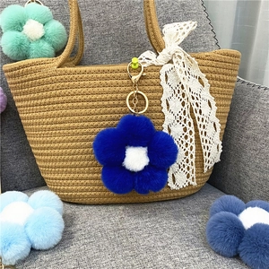 Detail of plush flower charm in teal blue hanging on a textured brown woven bag