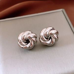 Macro shot of polished silver metal knot stud earrings on a textured grey display box