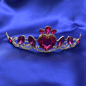 Close-up of golden princess crown with pink heart crystal on blue satin background