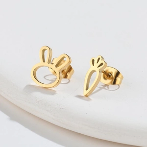 Macro shot of gold-plated asymmetric rabbit and carrot stud earrings on white stone
