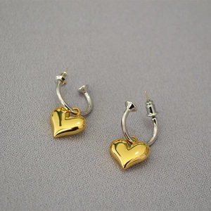 Detail shot of heart-shaped gold pendants with silver hoops on textured fabric
