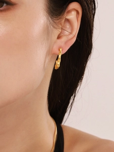 Macro shot of gold bamboo texture U-shaped geometric earrings on model's ear