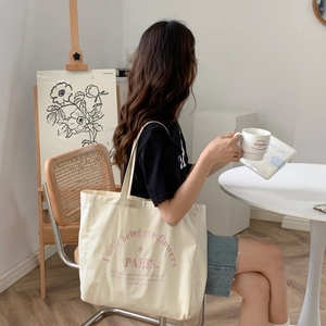 Close-up lifestyle view of a cream canvas tote bag featuring pink PARIS embroidery