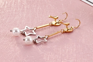 Détail macro de boucles d'oreilles étoile avec tiges dorées et perles blanches