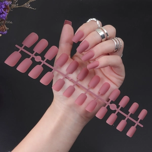 Detail of matte dark pink long square fake nails on runner with silver rings accessory