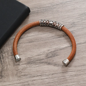 Detail of orange-brown braided leather bracelet with silver magnetic clasp and hollow metal charm