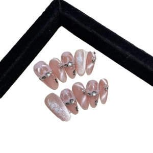 Pink cat eye press-on nails with floral art, pearls, and rhinestones set on white
