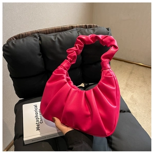 Detail of rose red pleated PU leather handbag on a textured dark chair with book prop