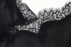 Detailed close-up of delicate eyelash lace trim and premium satin fabric on the black dress
