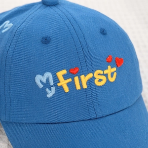 Detailed view of baby baseball cap with My First embroidery and red heart pattern