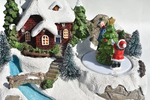 Détail d'une maison de Noël enneigée avec lumières LED, figurines et petits sapins