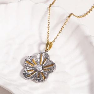 Détail d'un collier vintage à pendentif fleur et perle blanche sur un plateau blanc