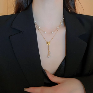 Collana a doppio strato con farfalla e perle dorate indossata da una modella in giacca