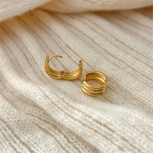 Close-up of triple-layered gold hoop earrings resting on a white knitted fabric background