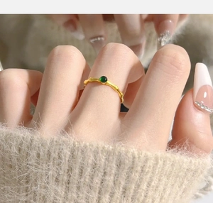 Close-up of a gold bamboo-shaped ring with a green jade bead on a model finger