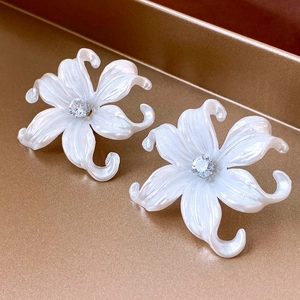 Close-up of white petal earrings with glossy texture and zircon center on gold tray