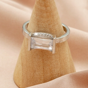 Detail of silver ring with rectangular zircon stone on a wooden stand with silk background