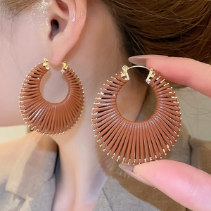Gros plan de créoles dorées recouvertes de cuir marron avec un design tressé texturé