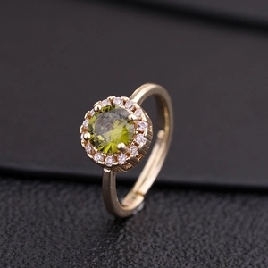Gros plan d'une bague dorée avec un grand zircon vert et halo de cristaux sur cuir noir