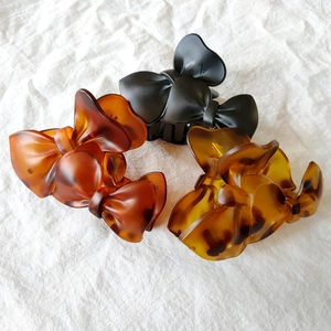 Close-up of three bow-shaped hair claws in black and amber leopard patterns on fabric