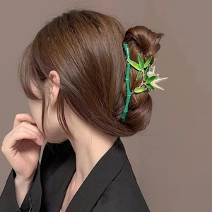 Detailed view of a green bamboo-shaped shark hair clip with a pearl on a model's hair