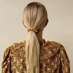 Gros plan d'un élastique à cheveux en métal doré torsadé porté sur une queue de cheval chic