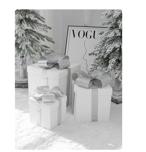 Three white decorative gift boxes with silver glitter bows in a snowy winter setting