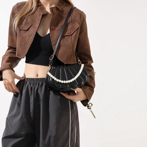 Detail of black shell-shaped crossbody bag with vertical texture and pearl chain handle