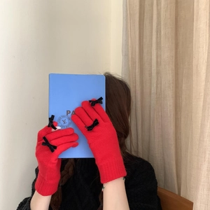 Detail of red knitted gloves with black bows on fingers held against a blue book
