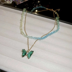 Detail of layered gold necklace featuring green butterfly pendant and crystal beads