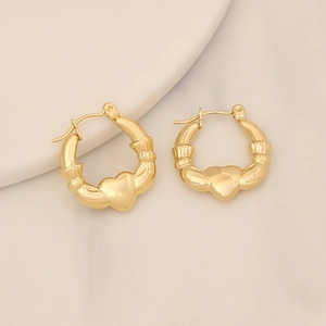 Orecchini Claddagh dorati minimalisti con design a cuore e mani su uno sfondo beige