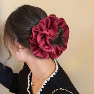 Elegant oversized burgundy satin scrunchie with ruffled pleats on model's low bun hairstyle