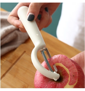 Close-up of a stainless steel peeler being used to skin a red apple in the kitchen