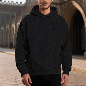 Men's solid black hooded sweatshirt featuring a jacquard texture in an outdoor street setting