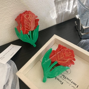 Elegant large rose flower hair claw clip with red petals and green leaves on black table
