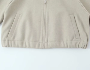 Détail d'un sweat à capuche beige avec fermeture éclair argentée et poches latérales