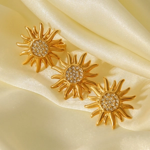 Detailed close-up of golden sun-shaped stud earrings with sparkling crystals on silk fabric