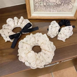Elegant white lace scrunchie set with black ribbon bow on a vintage wooden surface