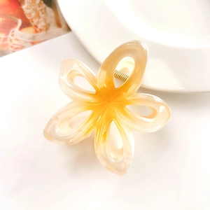 Macro detail of amber orange frangipani hair claw clip with golden metal spring