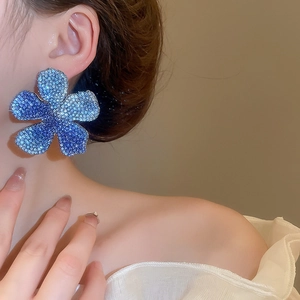 Detail of large oversized five-petal floral stud earrings with blue gradient crystal pavé